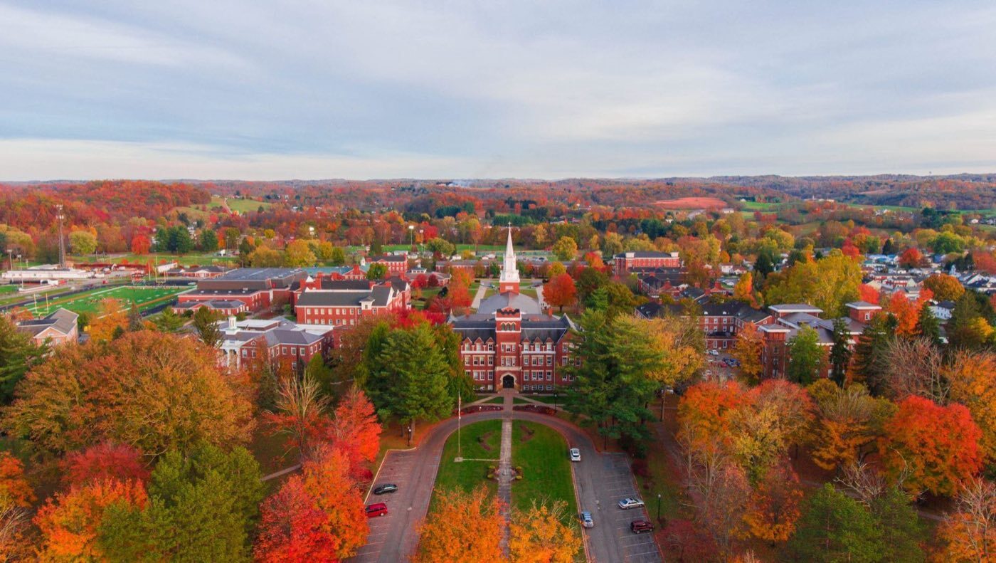 Aerial view of a small college campus in autumn, its white steeple rising above the quad